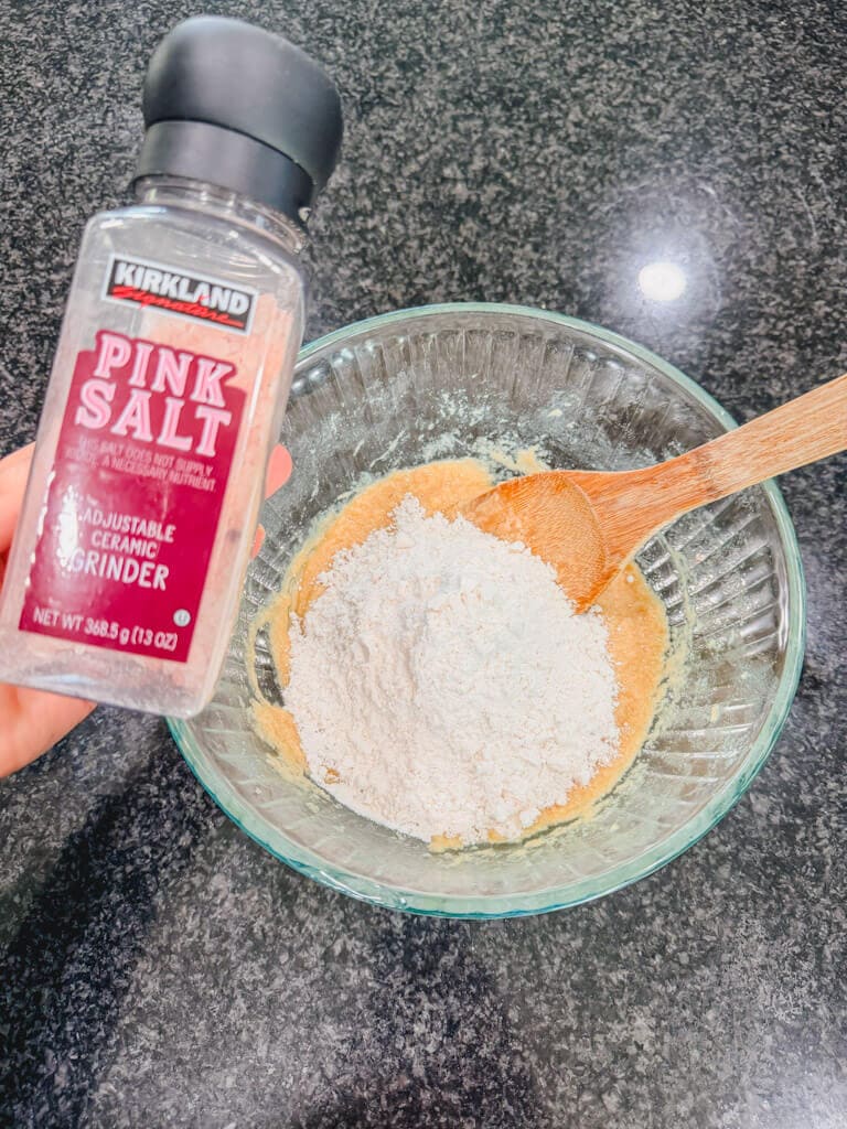 A jar of salt bean held over the mixing bowl of the wet ingredients, flour, and baking soda.