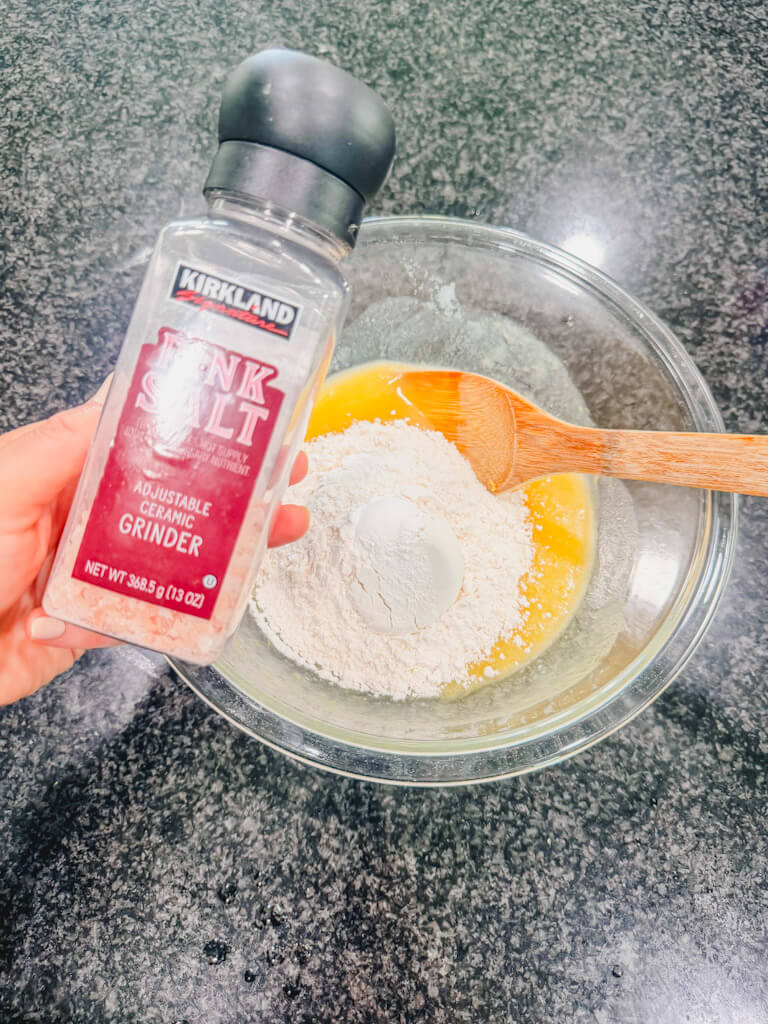 A bottle of pink salt being held over the mixing bowl.