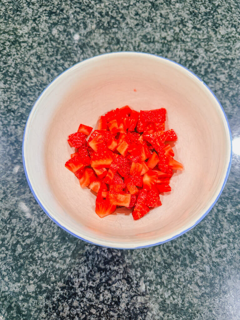 A small blue bowl of diced strawberries on a black counter.