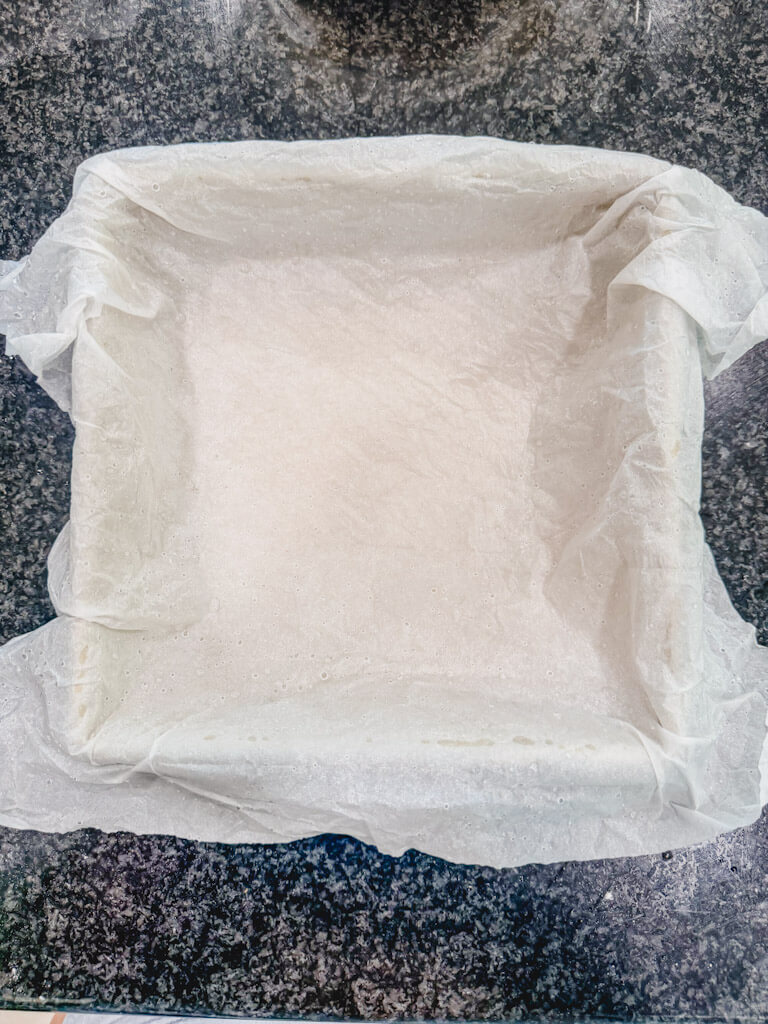 An 8 x 8 baking dish with parchment paper on a black countertop.