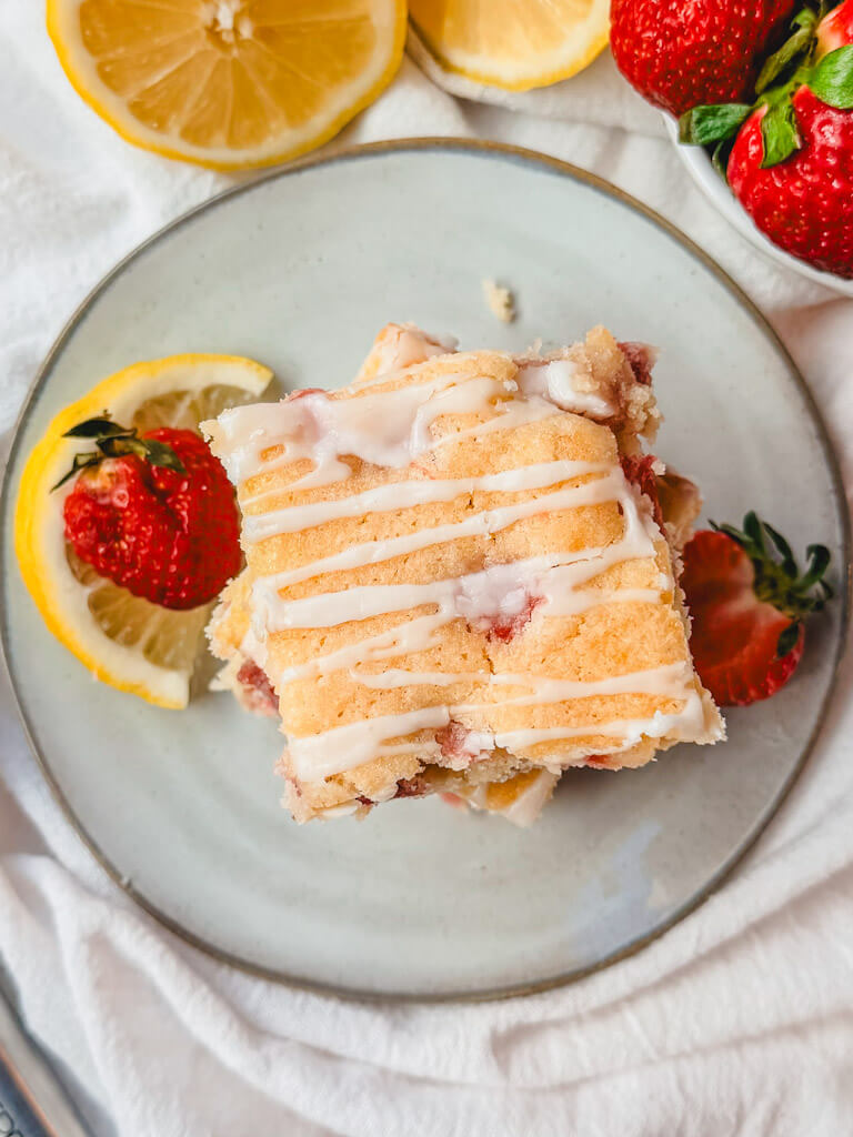overhead view of a strawberry lemon bar on a plate with strawberries and lemon slices on the plate.