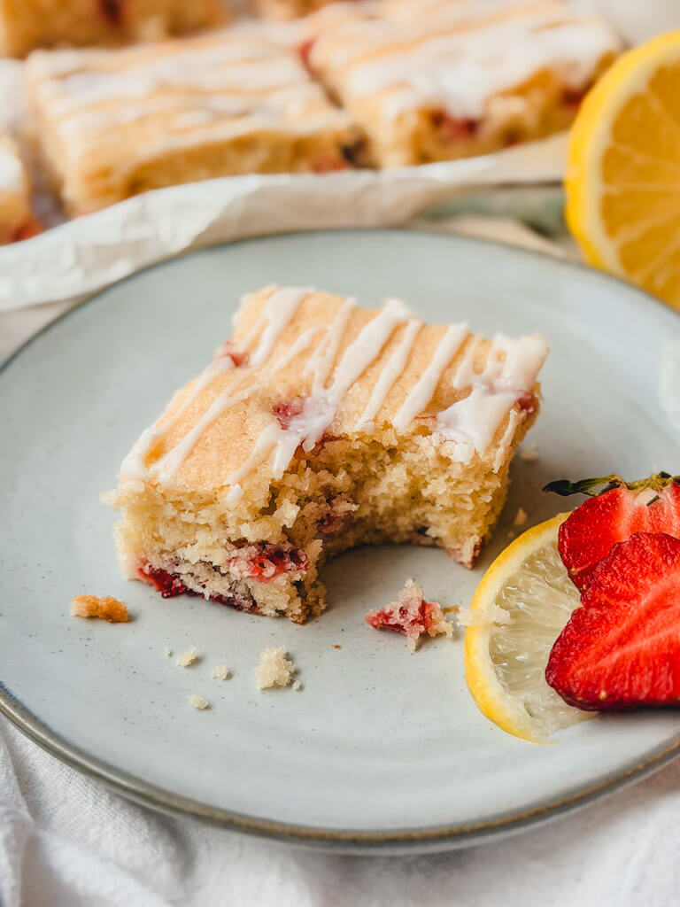 close up of a strawberry lemon bar with a bite that has been taken out of it on a plate.