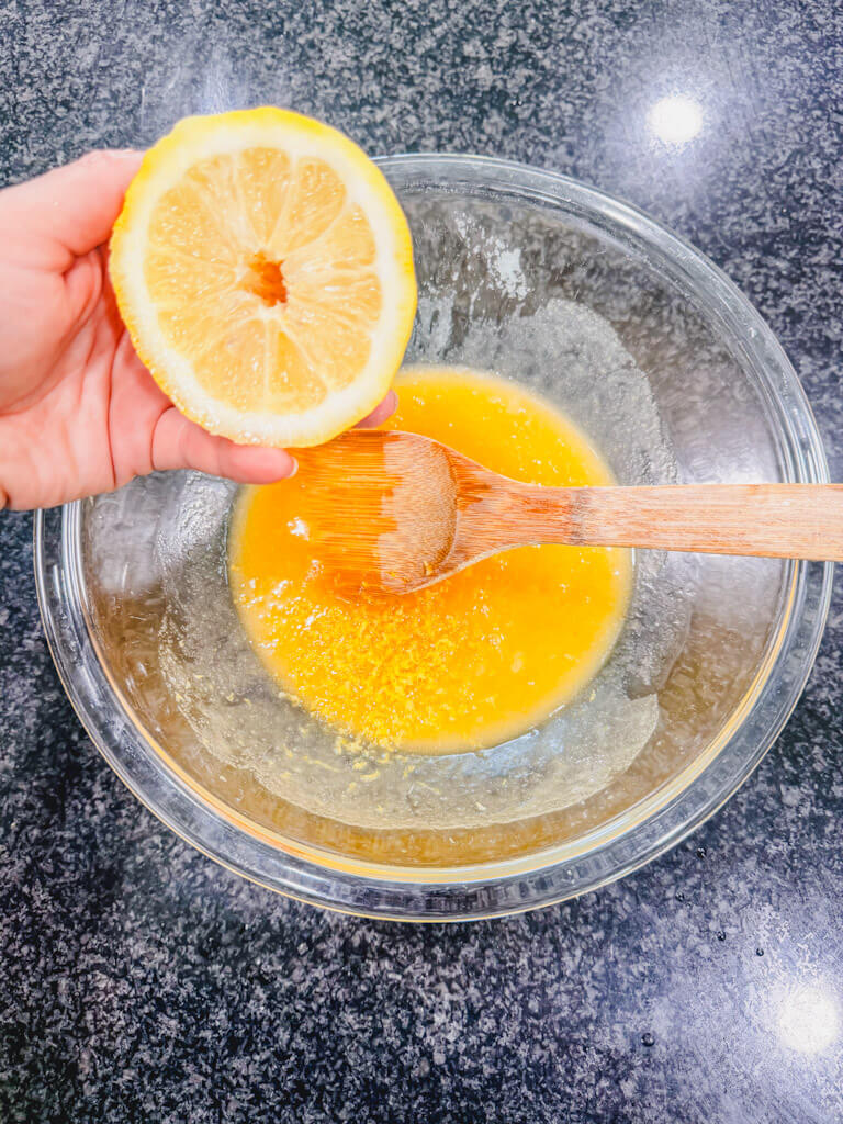 Half of a lemon being held over the mixing bowl.