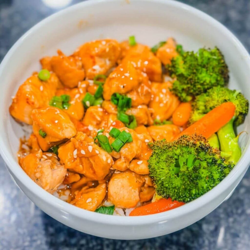 Teriyaki chicken in a bowl over white rice with roasted broccoli and carrots next to it.