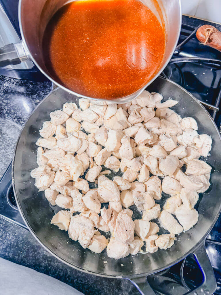 The saucepan with teriyaki sauce about to be poured into the chicken that is cooking in the skillet.