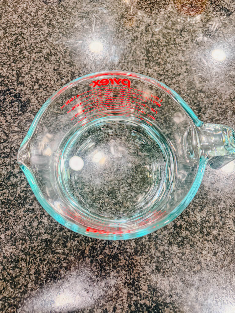 Measuring water in a glass measuring cup for homemade teriyaki sauce on a black counter.