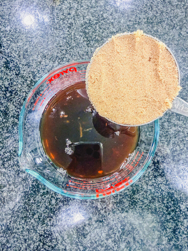 Brown sugar being added to teriyaki sauce mixture for sweetness.