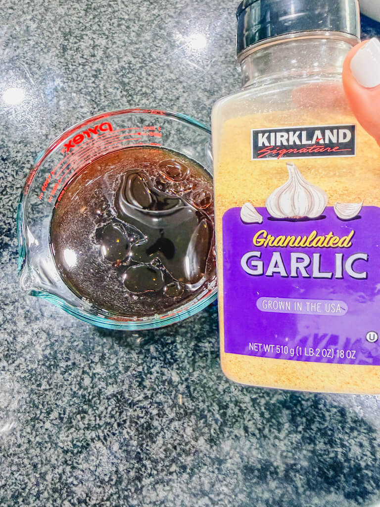 A bottle of garlic powder being held over the glass measuring cup.