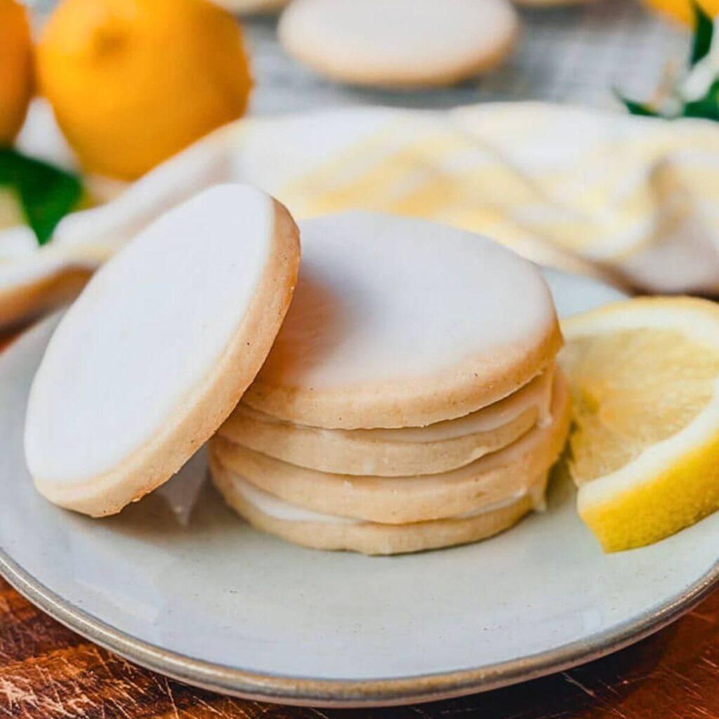 a stack of iced lemon vanilla bean shortbread cookies on a white plate, with one cookie leaning against the stack.