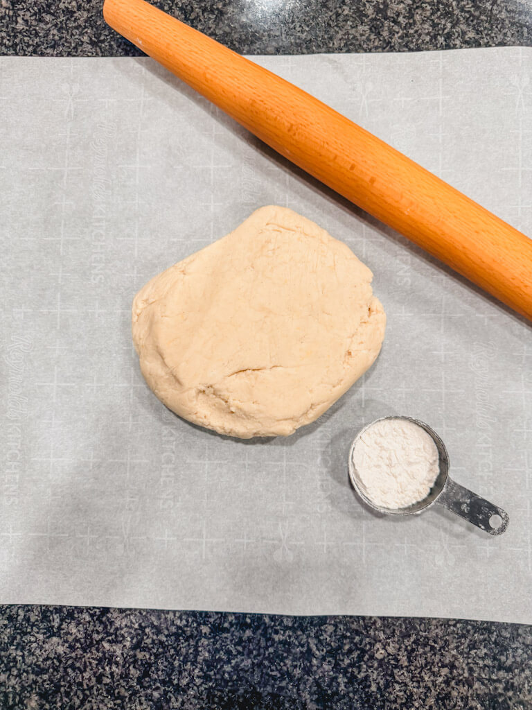 Cookie dough on top of a piece of parchment paper next to a rolling pin and some flour.