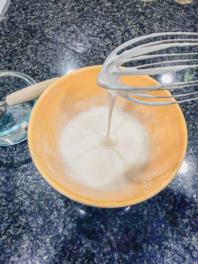 Close-up of the lemon glaze dripping off of a whisk.