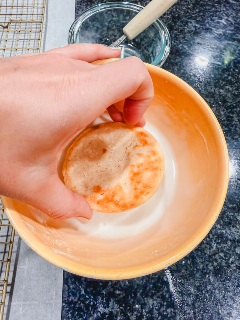A hand holding a cookie dipping it into the glaze.