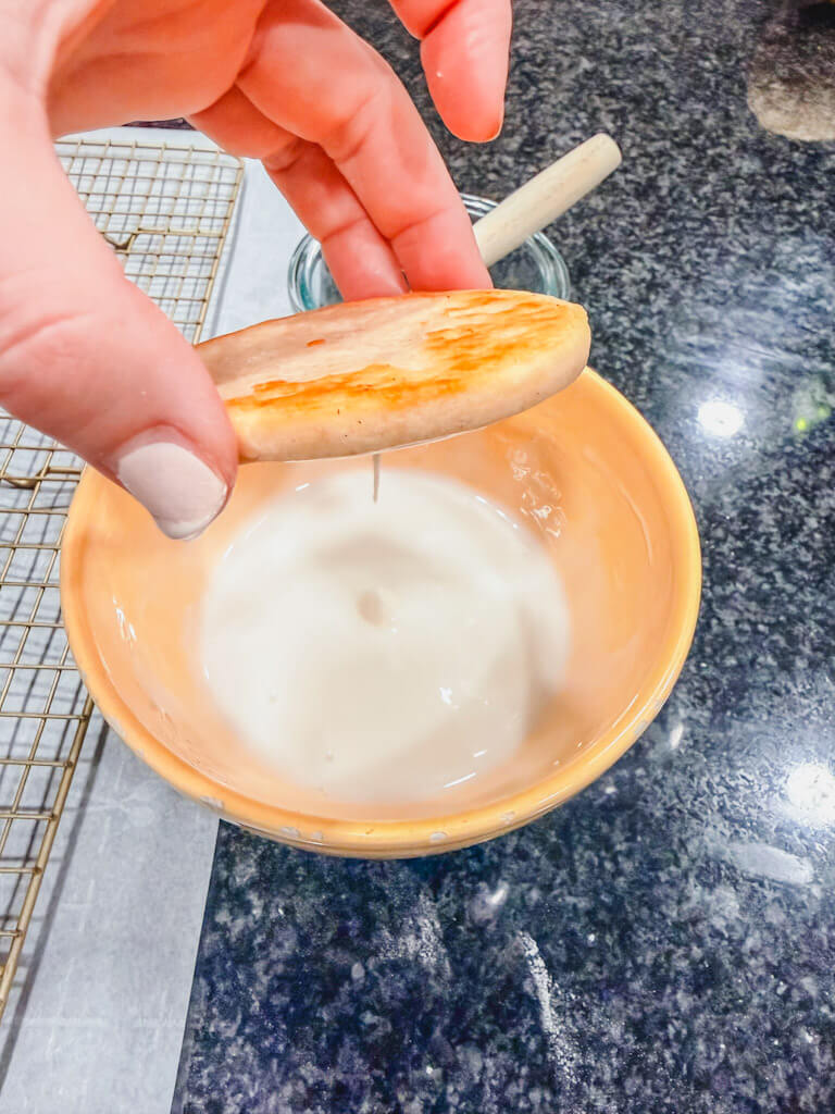 A hand holding the glazed cookie over the frosting bowl.