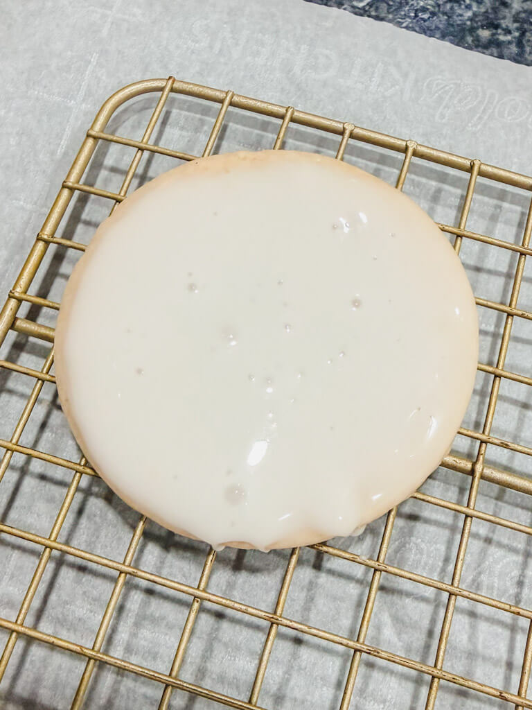 close up of a cookie on a wire rack, allowing the excess glaze to drip off the cookie.