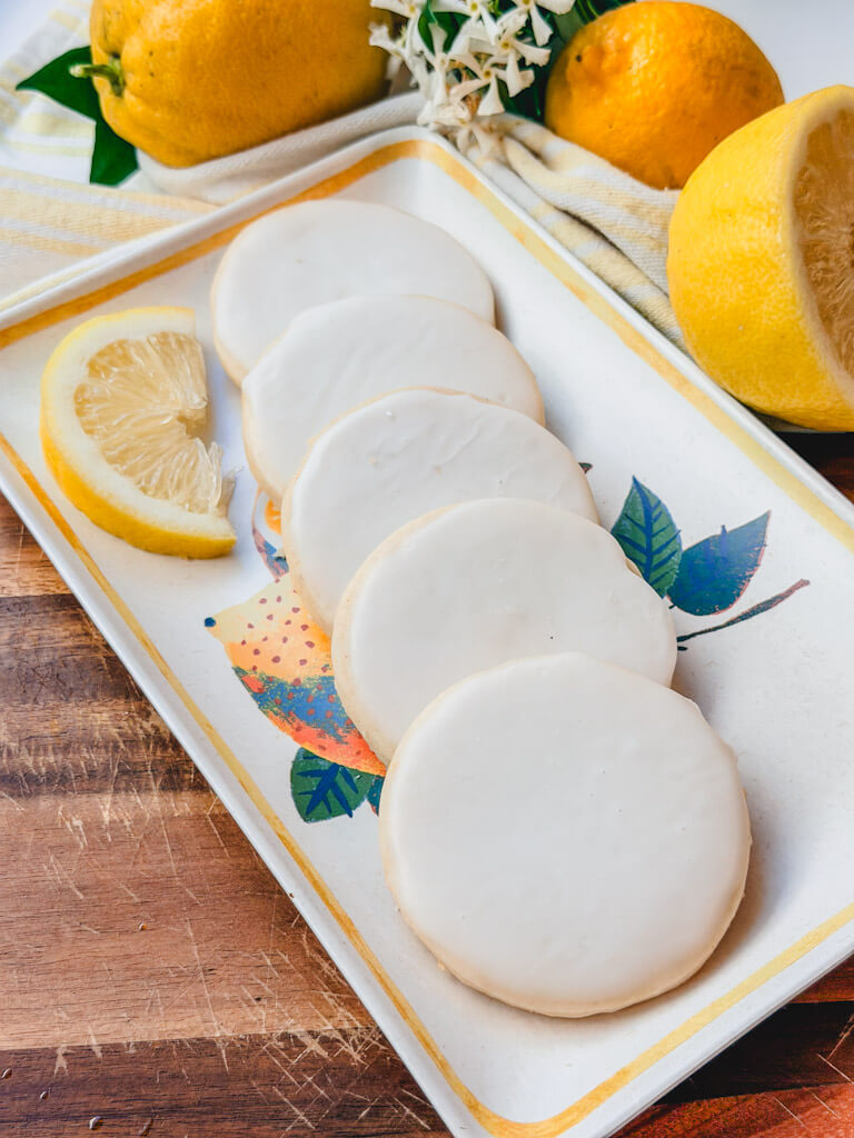 Iced lemon vanilla bean shortbread cookies arranged on a lemon-themed serving tray with fresh lemons in the background.
