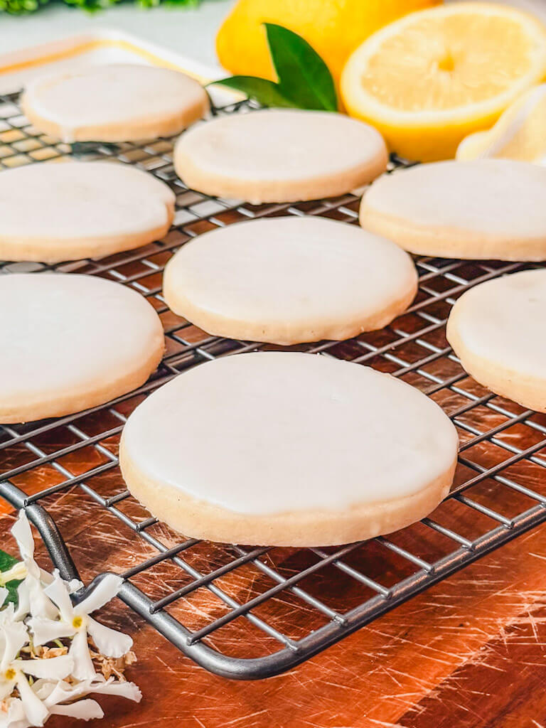 Iced lemon vanilla bean shortbread cookies on a wire rack with fresh lemons in the back.