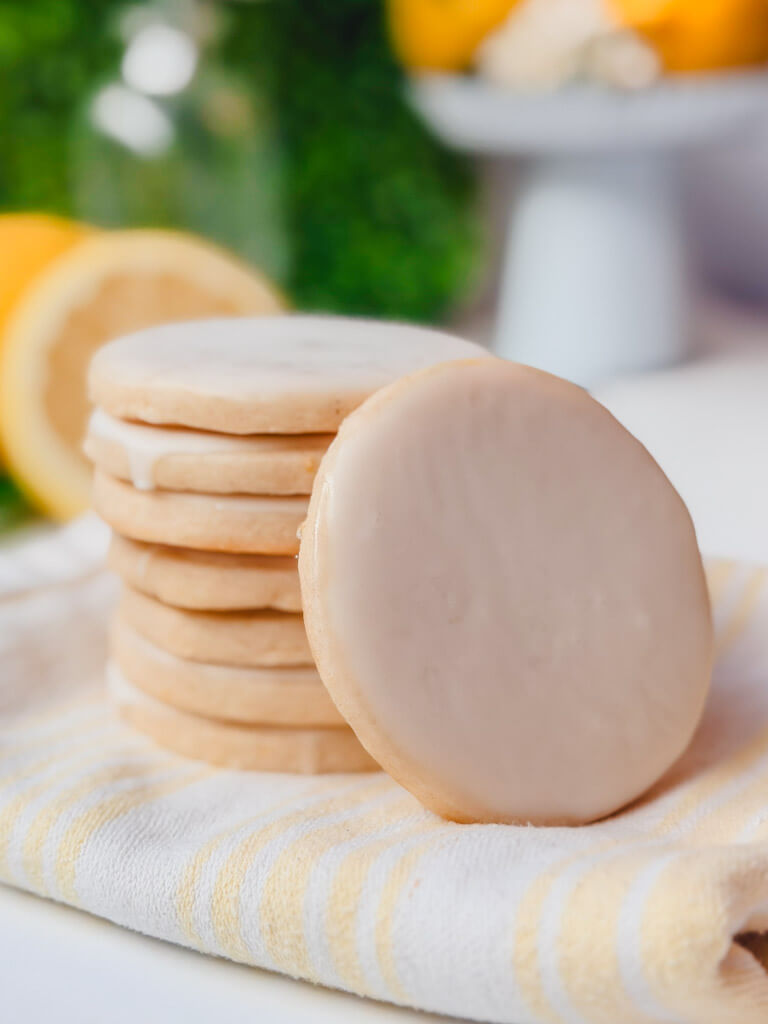 Lemon vanilla bean shortbread cookies stacked on a striped kitchen towel with lemons in the background.