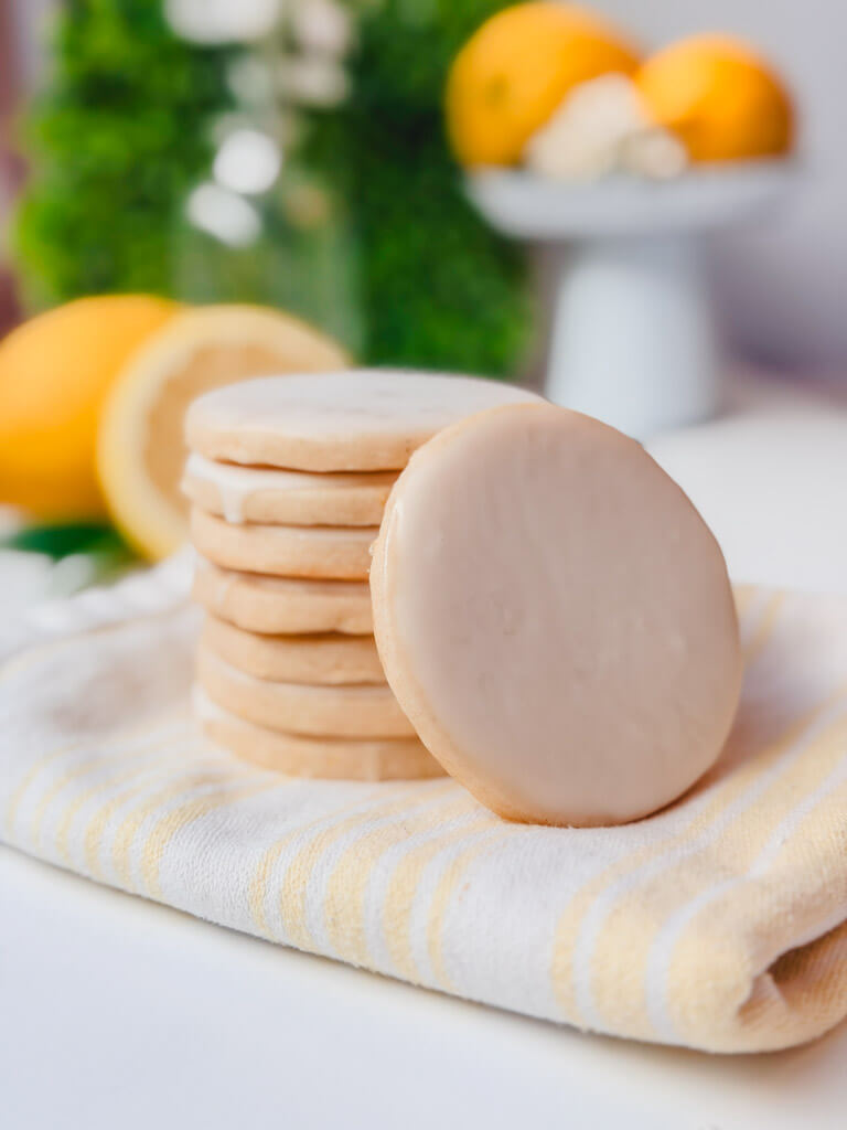 Bakery-style iced lemon vanilla bean shortbread cookies styled with lemons and a striped kitchen towel.
