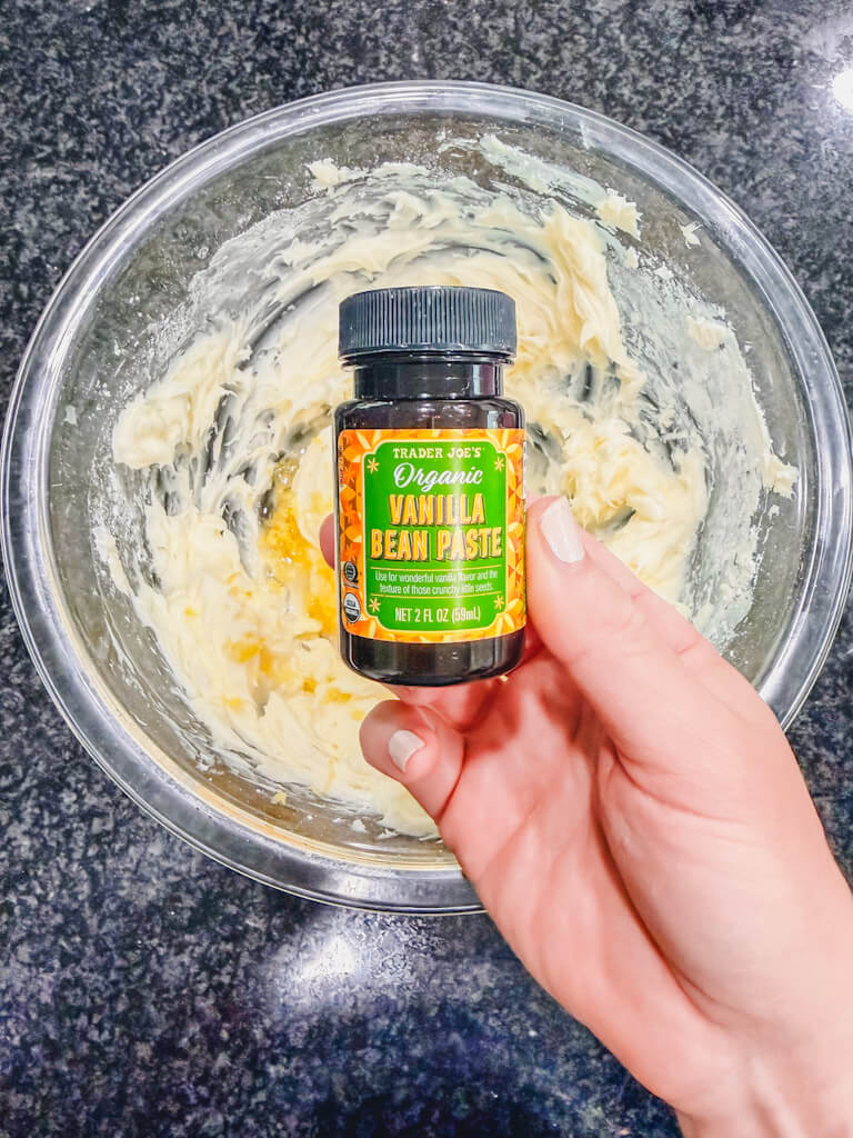A bottle of vanilla bean paste being held over the butter and sugar mixture.