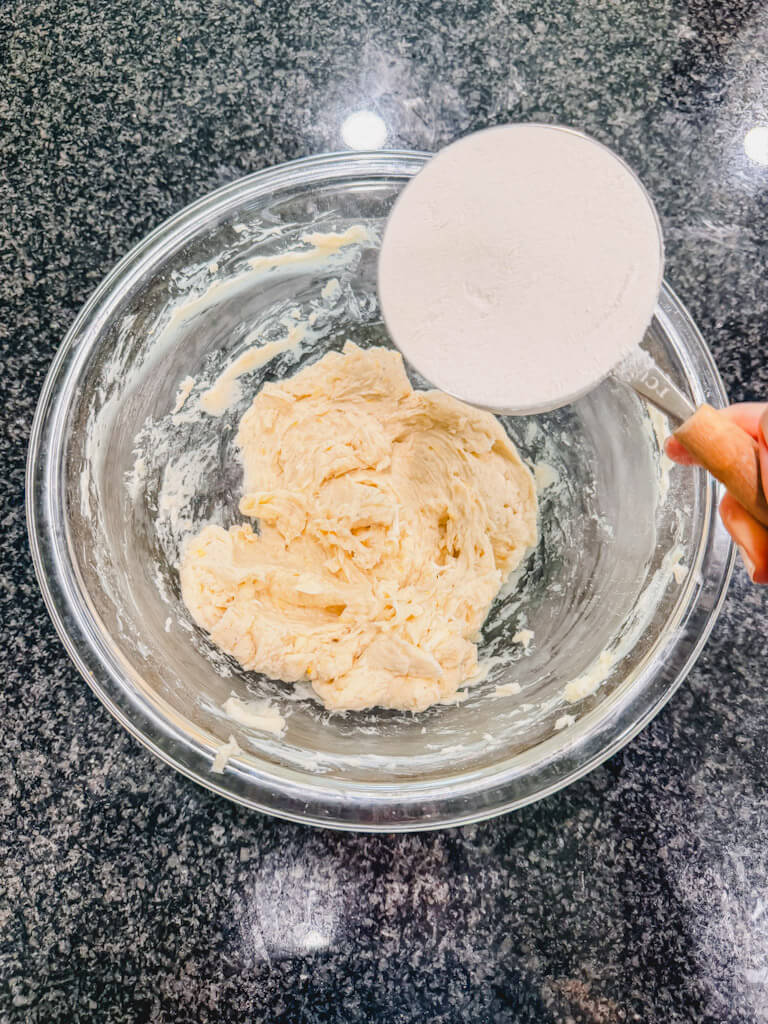 A measuring cup, holding flour over the mixing bowl for the lemon vanilla bean shortbread cookies.