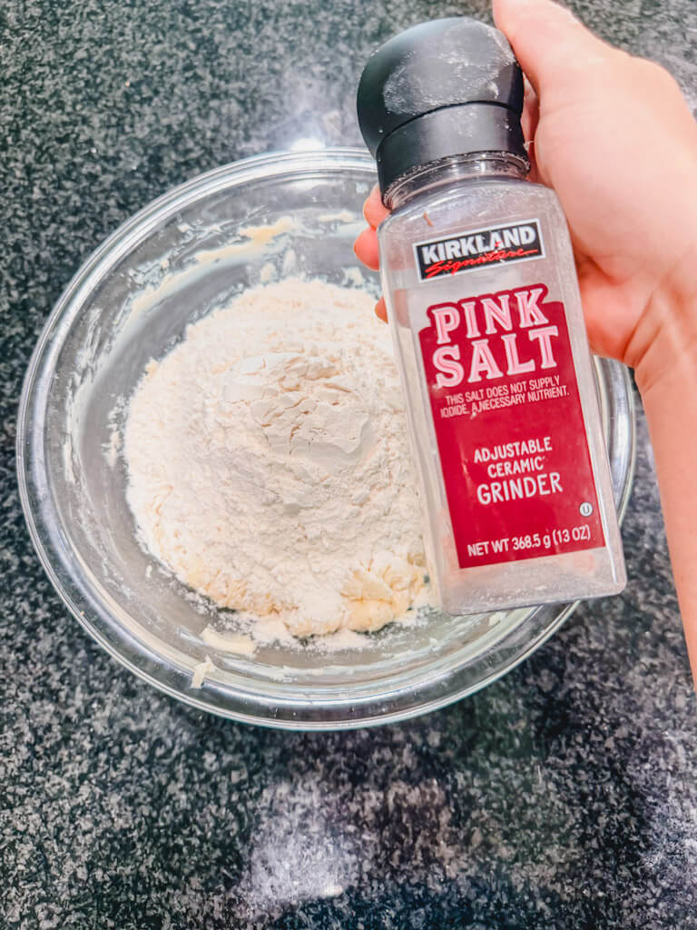 A bottle of pink salt being held over the mixing bowl.