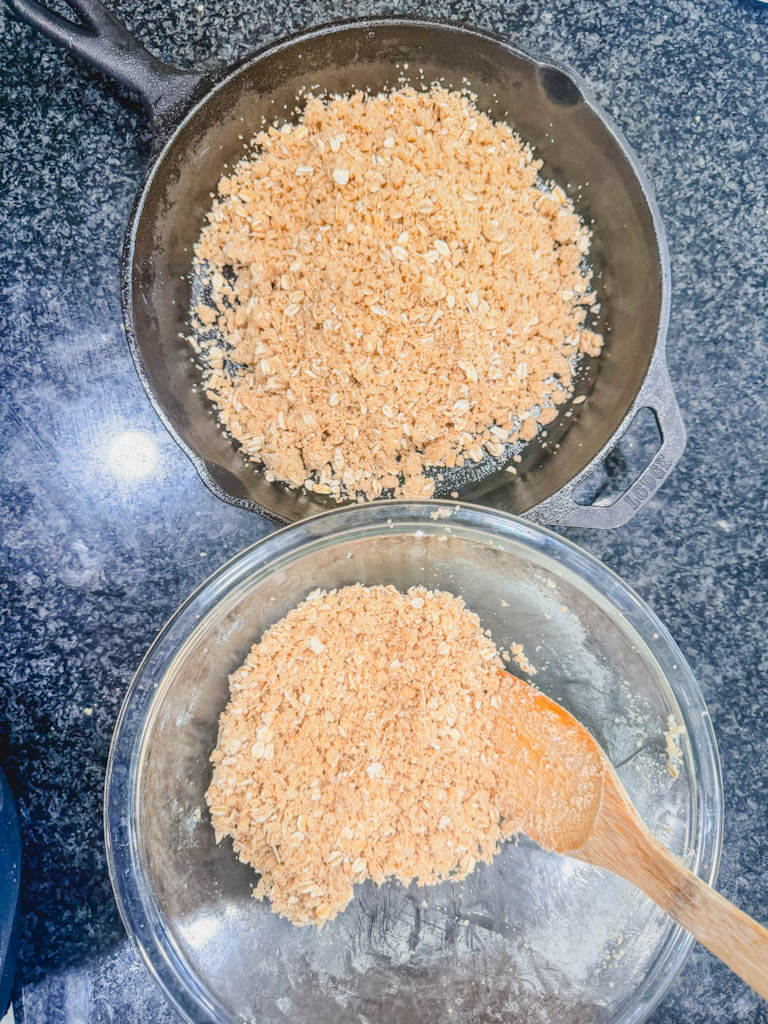 Graham cracker crumble mixture being divided between a mixing bowl and a greased cast iron skillet.