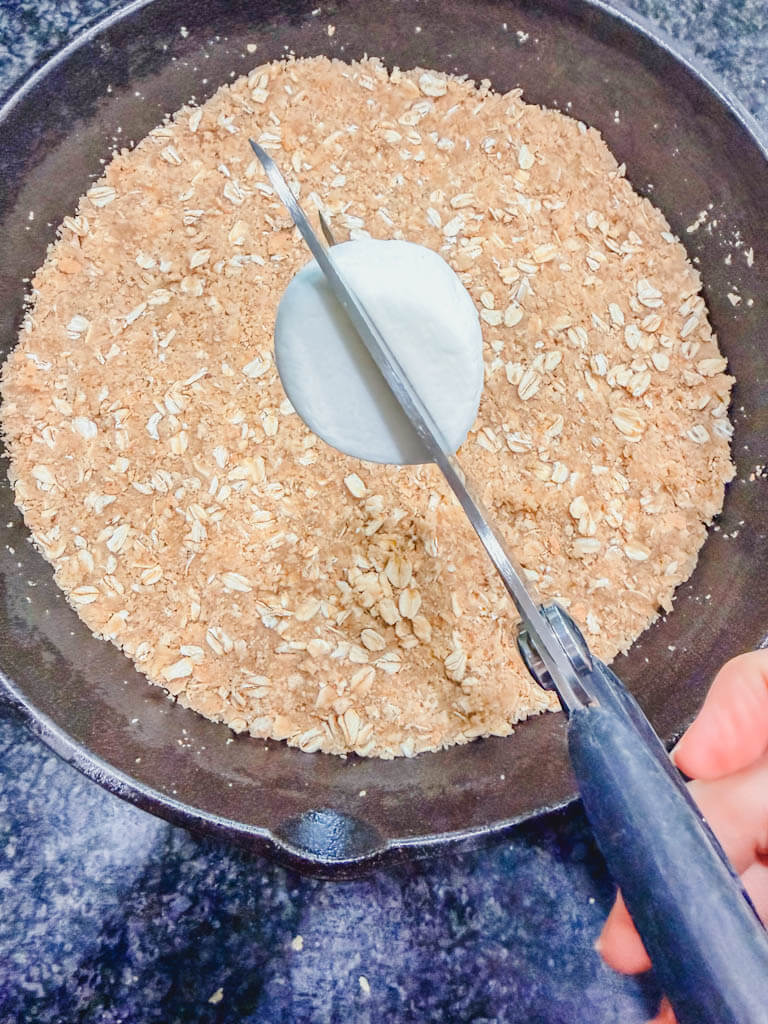 A large marshmallow being cut in half with kitchen scissors over a graham cracker crust.