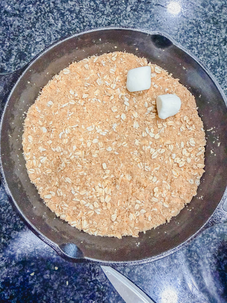 Halved marshmallows being arranged on top of the graham cracker crust in a cast iron skillet.