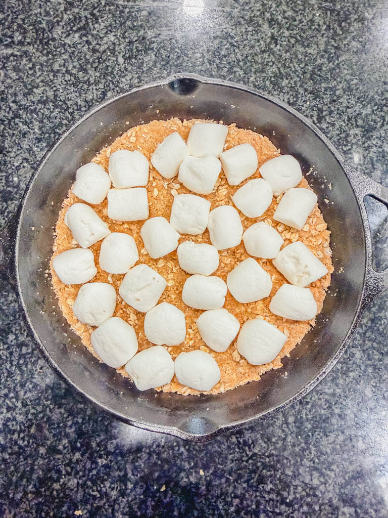 A single layer of halved marshmallows arranged over the graham cracker crust in a cast iron skillet.