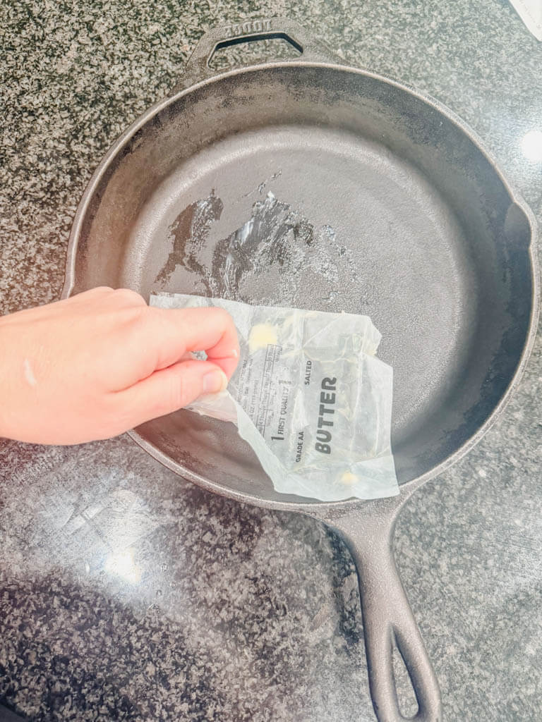 A cast iron skillet being greased with a butter wrapper before making Cast Iron Skillet S'mores Pie.