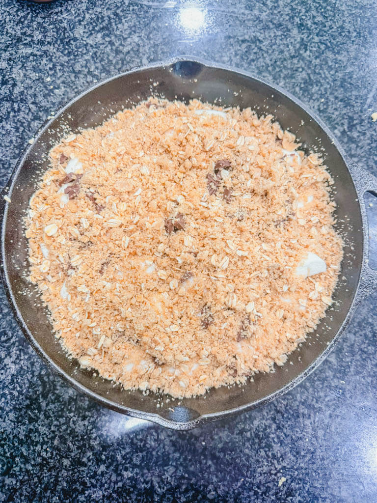 Remaining graham cracker crumble mixture sprinkled over the marshmallow and chocolate filling in a cast iron skillet.