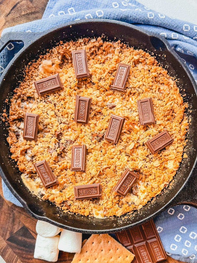 Overhead shot of pie on a wooden cutting board next to marshmallows, chocolate, and graham crackers.