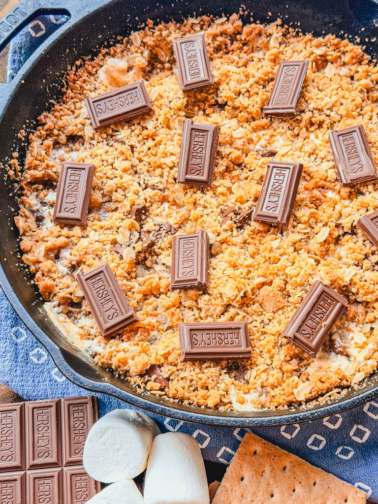 Overhead view of Cast Iron Skillet S'mores Pie garnished with chocolate pieces, graham crackers, and marshmallows.