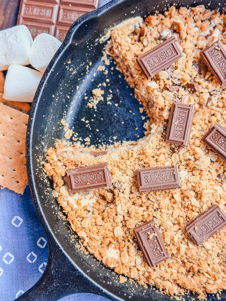 Cast Iron Skillet S'mores Pie with a serving removed and chocolate pieces on top.