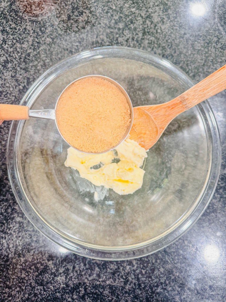 Brown sugar being added to softened butter in a glass mixing bowl.