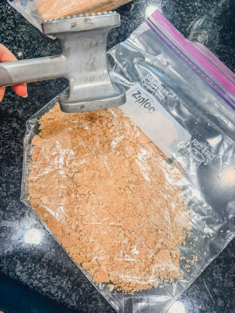 Graham crackers crushed into fine crumbs inside a zip-top bag using a meat mallet.