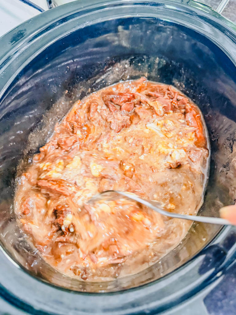 a spoon stirring the cream cheese and sour cream into the beef.