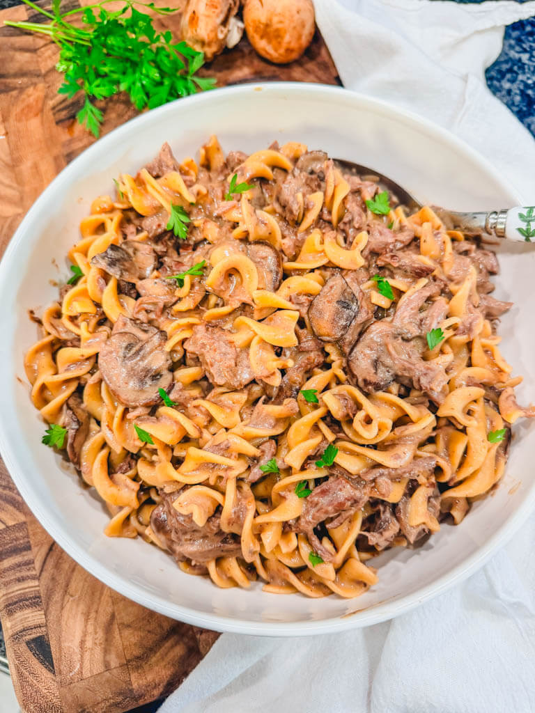 overhead view of beef stroganoff in a white serving bowl next to a white colored kitchen towel.