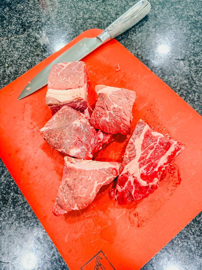large chunks of beef chuck on a red cutting board.