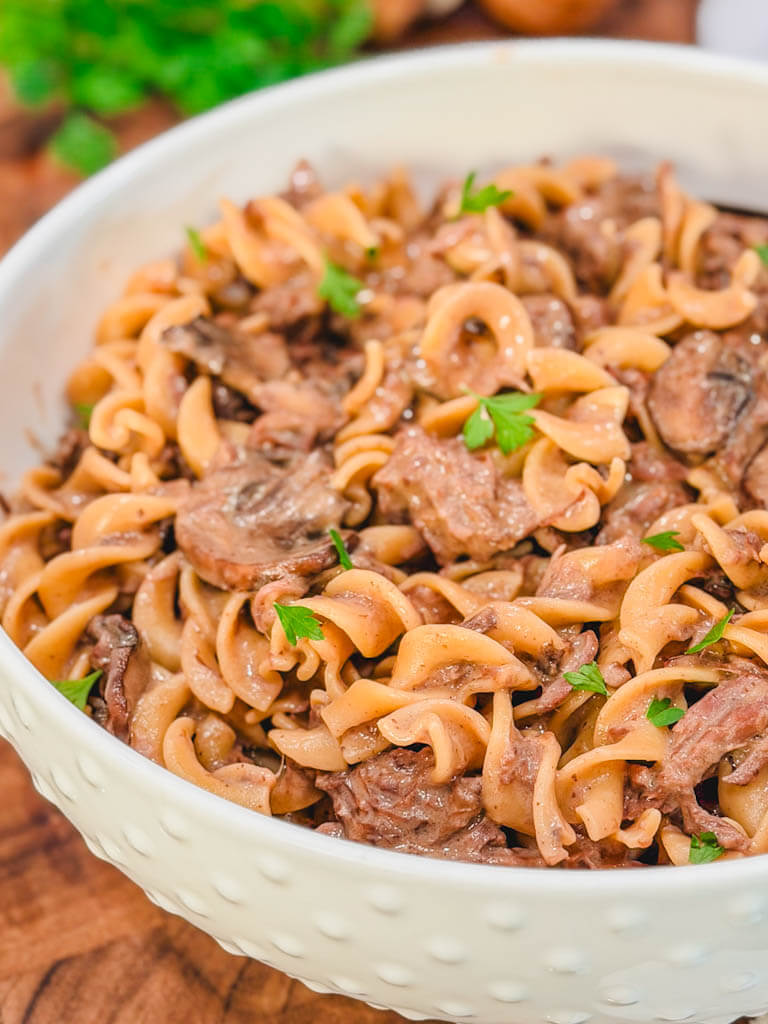 close up of beef stroganoff in a white pasta serving bowl.