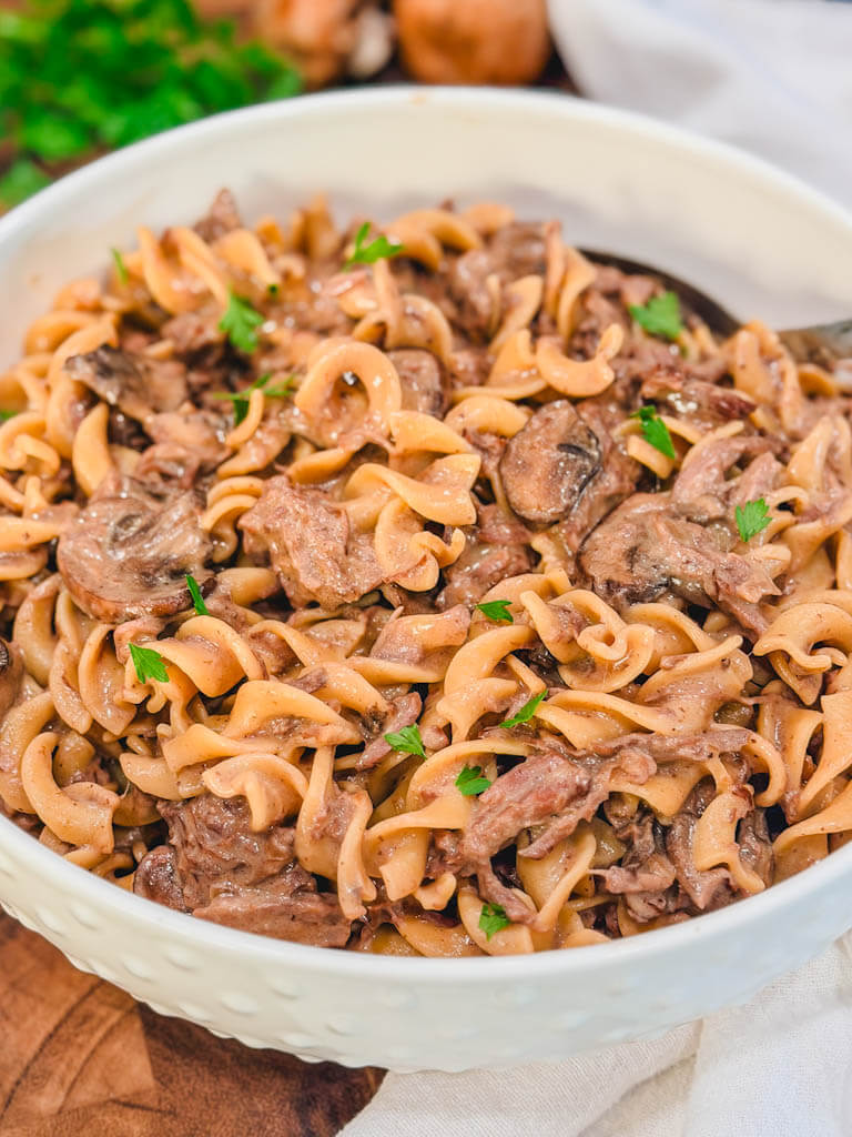 slow cooker beef stroganoff on top of a wooden cutting board.