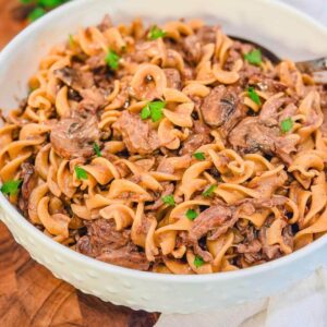 Slow Cooker Beef Stroganoff in a large white serving bowl with fresh parsley on top.