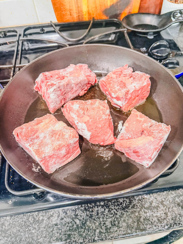 floured beef chuck chunks searing in a cast iron skillet with olive oil.
