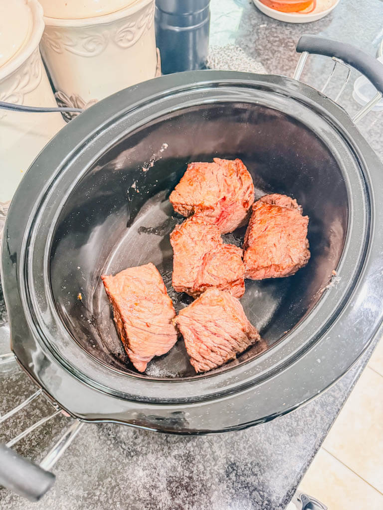 browned beef chunks placed into a slow cooker.