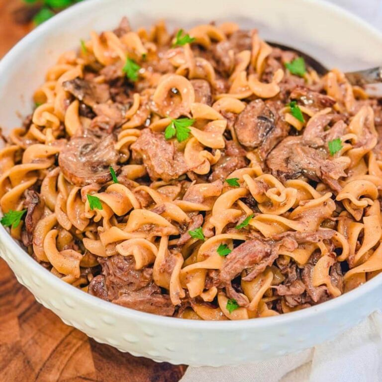 Slow Cooker Beef Stroganoff in a large white serving bowl with fresh parsley on top.