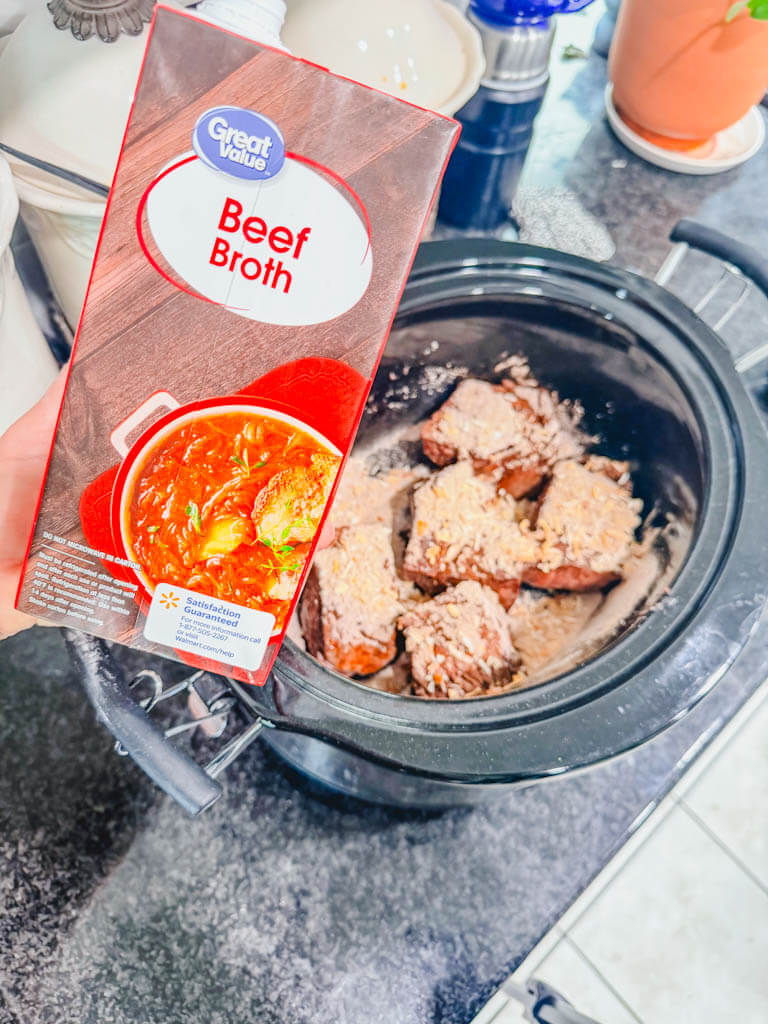 a box of beef broth being held over the slow cooker.
