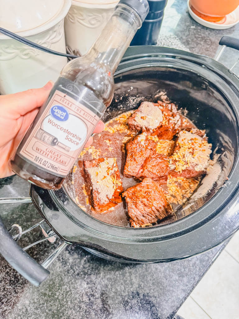 a bottle of Worcestershire sauce being held over the slow cooker.