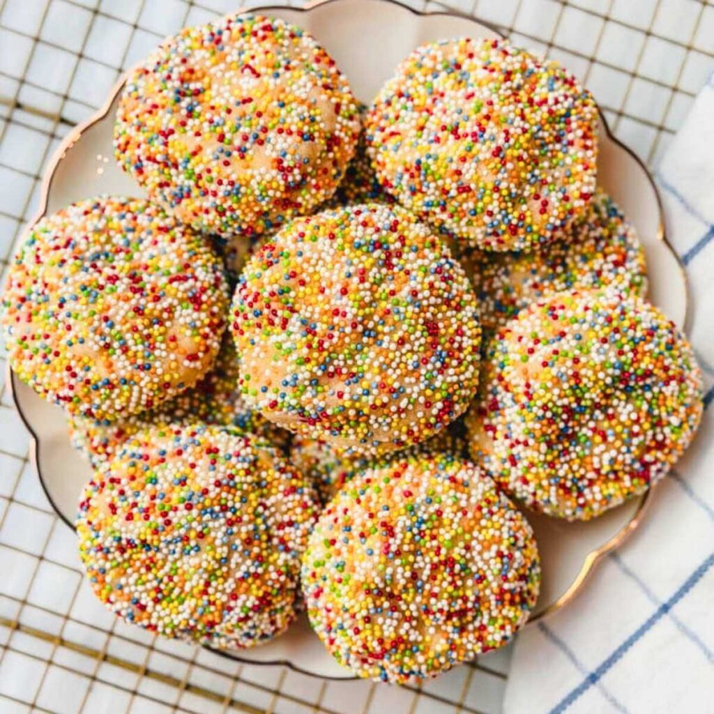 Sprinkle sugar cookies on a plate on top of a wire rack next to a blue striped kitchen towel.