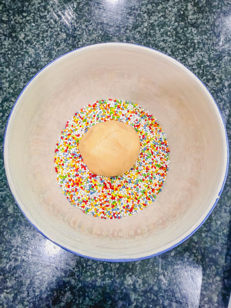 a cookie dough ball added to the bowl of sprinkles.
