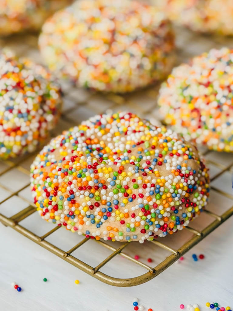 close up of a sprinkle sugar cookie on a wire rack with sprinkles underneath the rack.